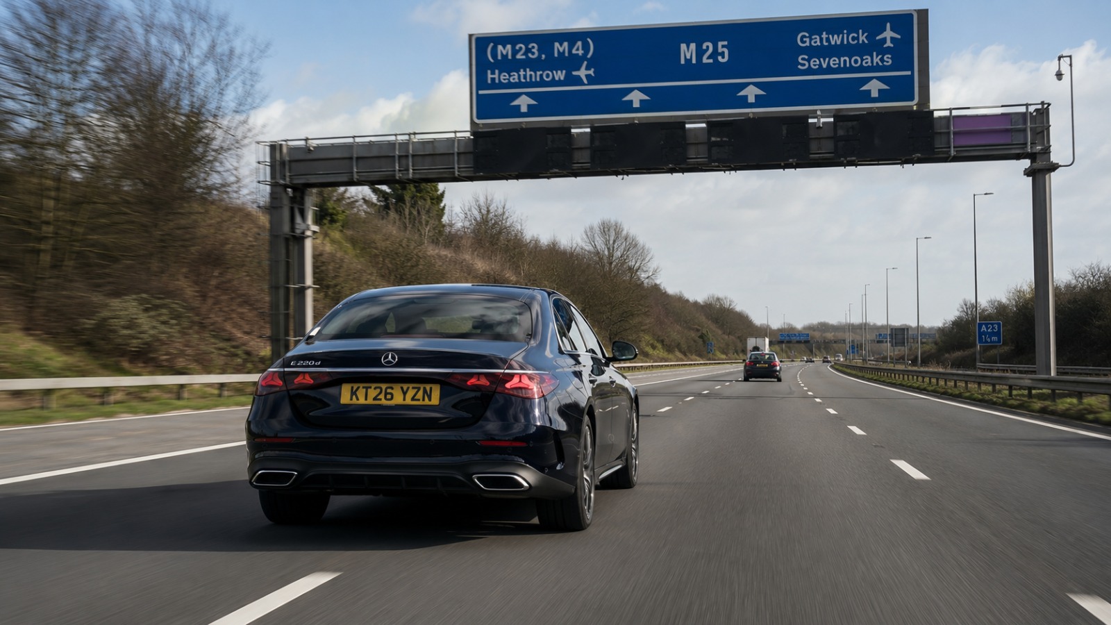 Dark executive saloon on the M23 motorway heading north from Gatwick toward London under daytime sky