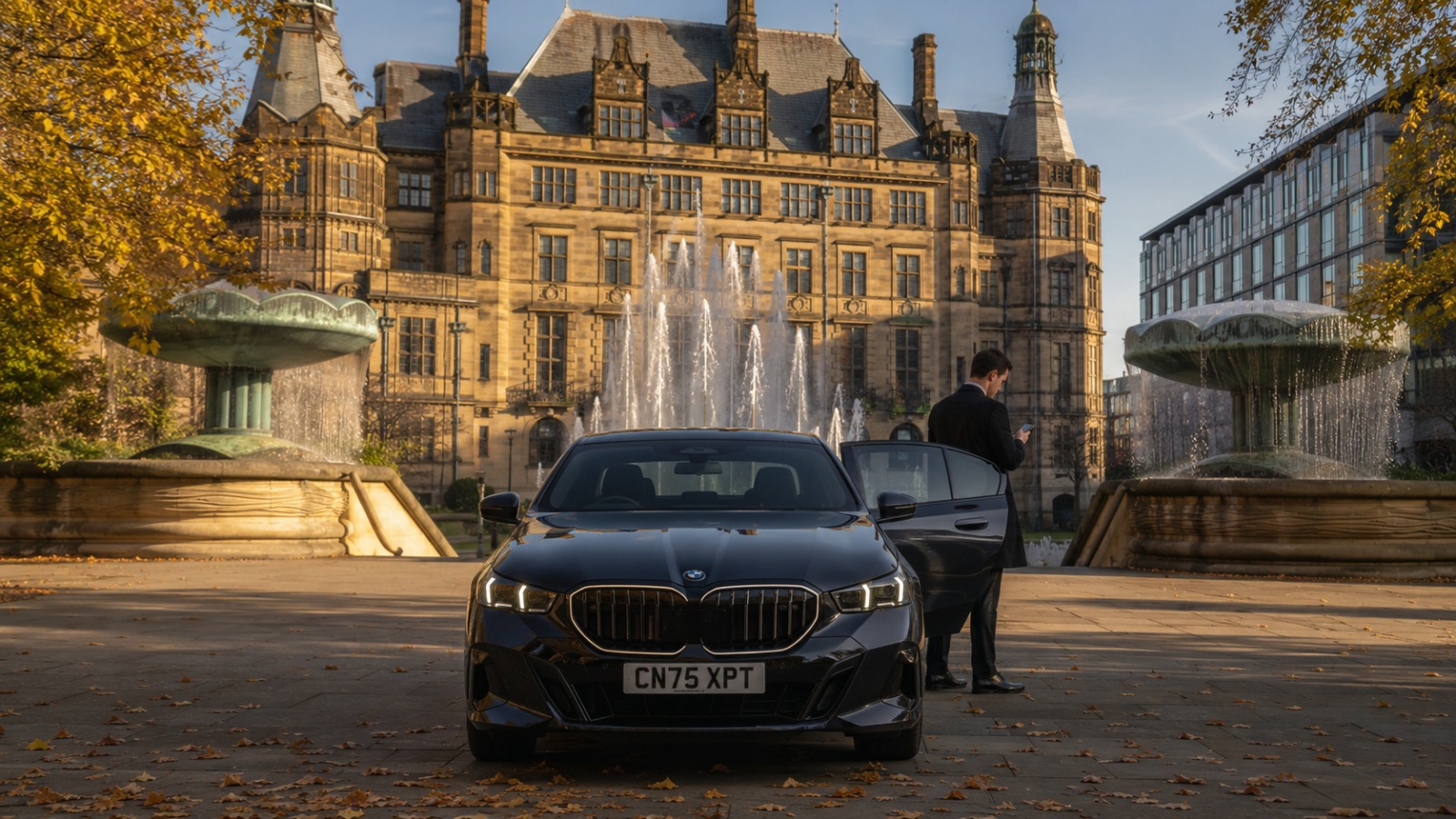 BMW saloon at Sheffield Peace Gardens fountains in autumn morning light for Manchester Airport departure