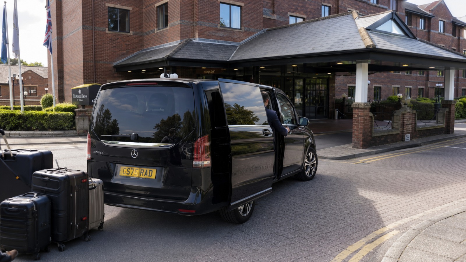 Driver closing sliding door on family group boarding 8-seat minibus at Stoke-on-Trent hotel for Manchester Airport