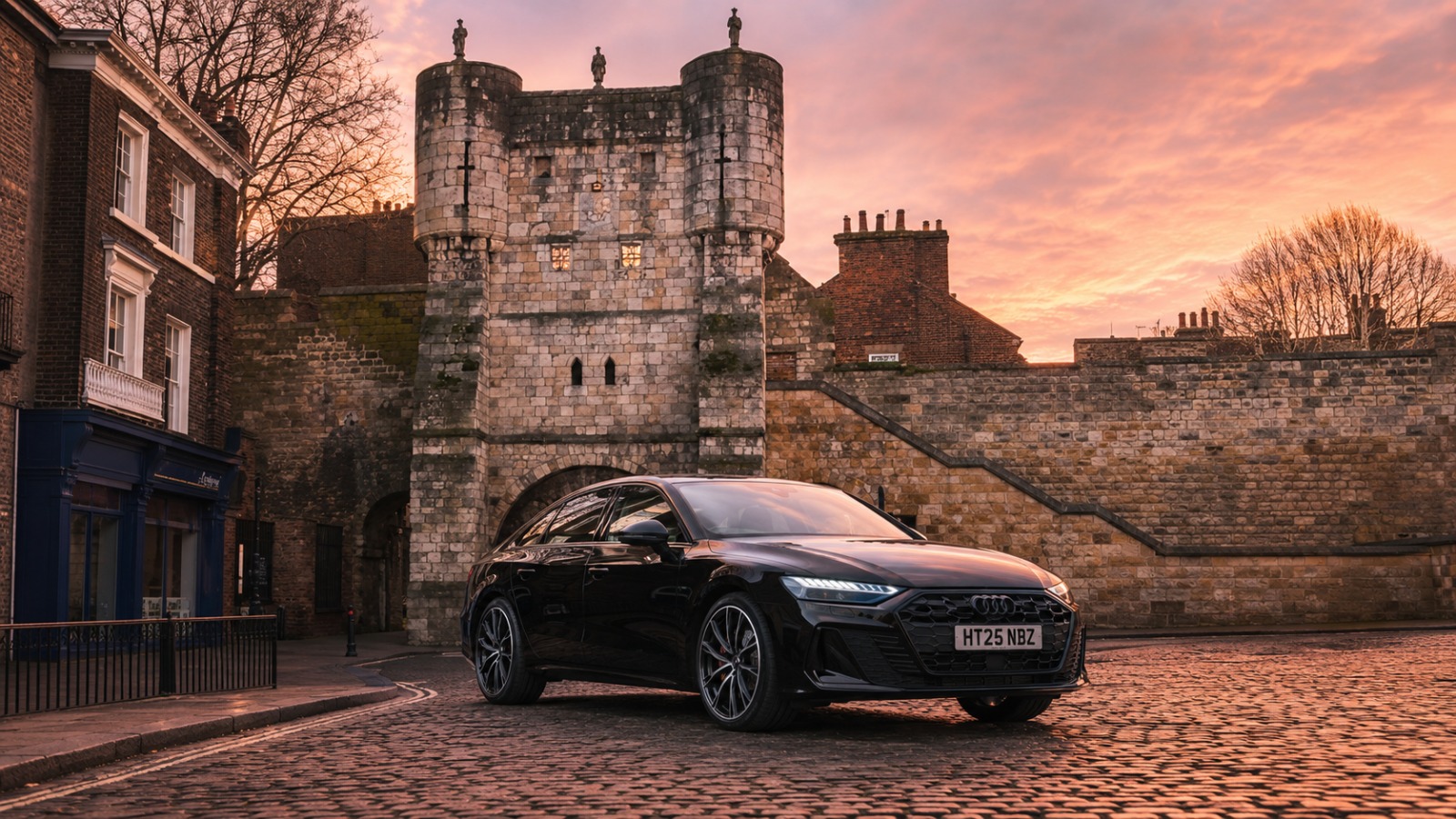 Executive Audi saloon at sunrise on cobbles below York medieval City Walls for Manchester Airport departure